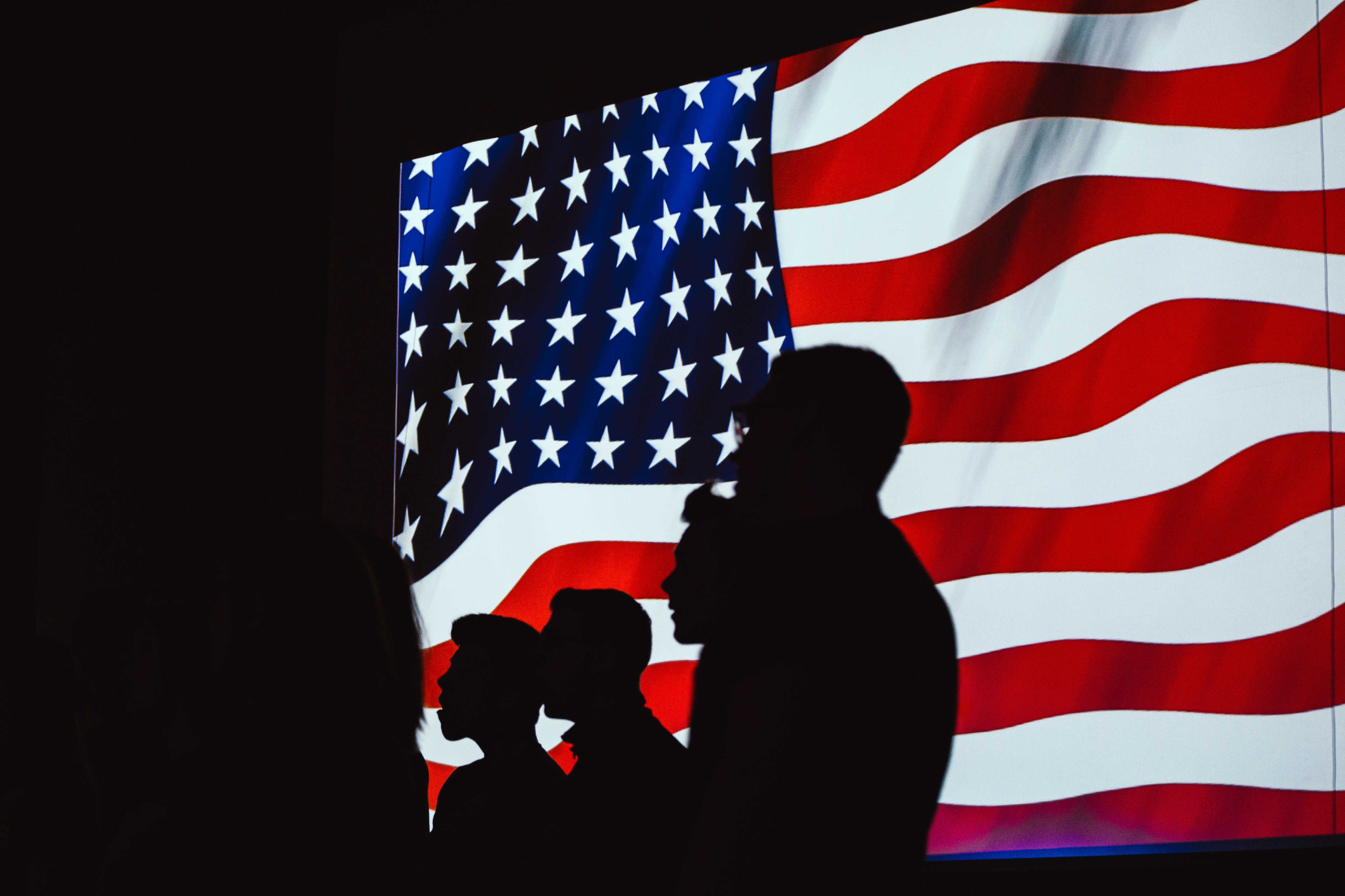 People in silhouette standing in front of a giant screen with an American Flag waving